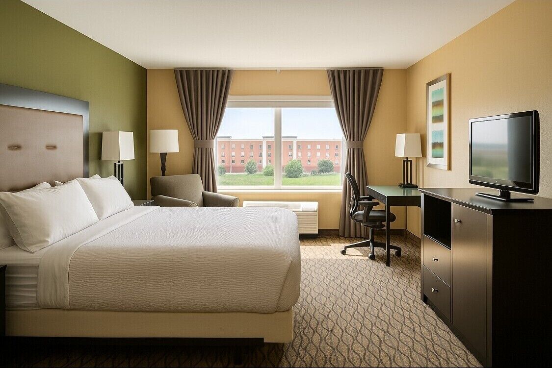 A hotel room with a bed, desk, chair, TV, and a window with curtains.