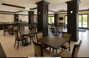 Un vaste espace dédié à la salle à manger, avec de grandes tables et des chaises hautes, de larges piliers et un comptoir équipé d’une machine à café.