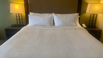 A neatly made bed with white linens, two bedside tables with lamps, and a wall-mounted telephone.