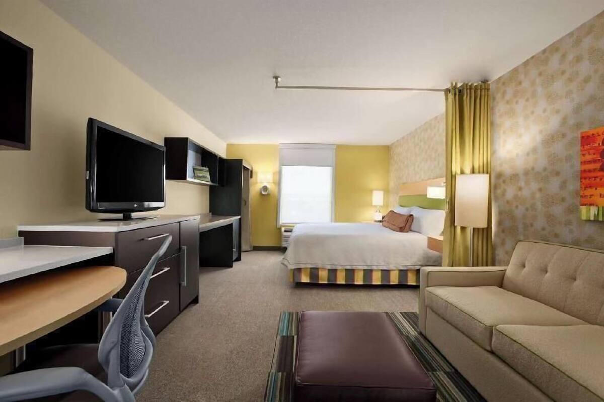 Une chambre d’hôtel avec un lit, un bureau avec une télévision, un canapé et une fenêtre.