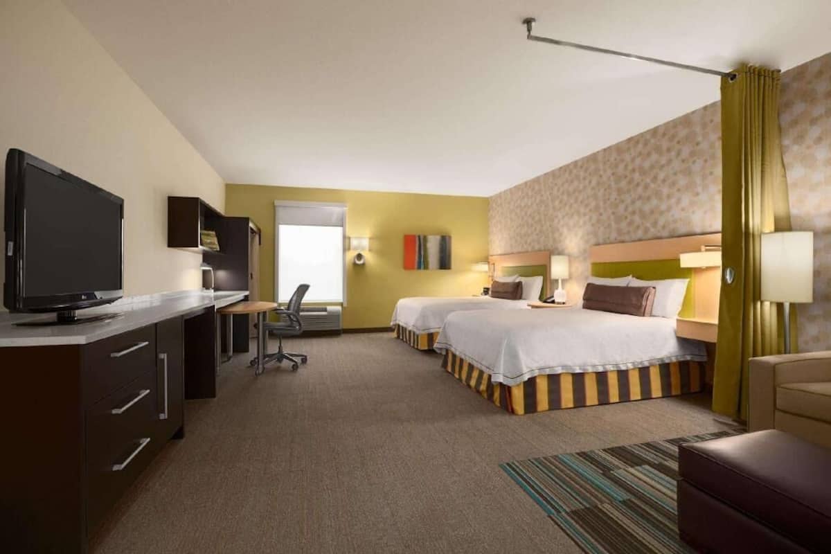 Une chambre d’hôtel avec deux lits, un bureau avec une télévision, une chaise et une lampe de bureau.