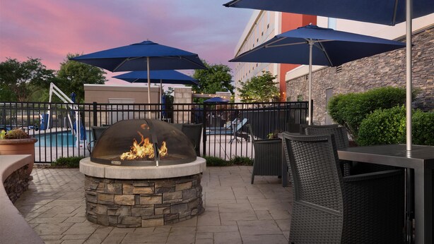 Eine Außenpatio-Terrasse mit einem Steinkamin, Sitzgelegenheiten im Freien, Sonnenschirmen und einem Pool im Hintergrund.