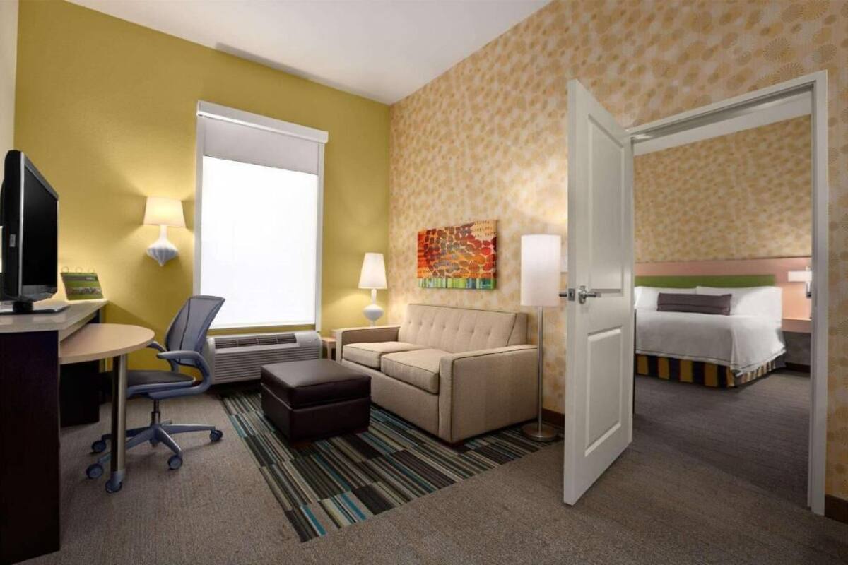 Une chambre d’hôtel équipée d’un bureau, d’une chaise, d’un canapé, d’un pouf, d’un lit et d’un tableau au mur.