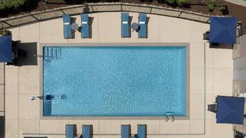 An aerial view of a rectangular swimming pool with lounge chairs and umbrellas around it.