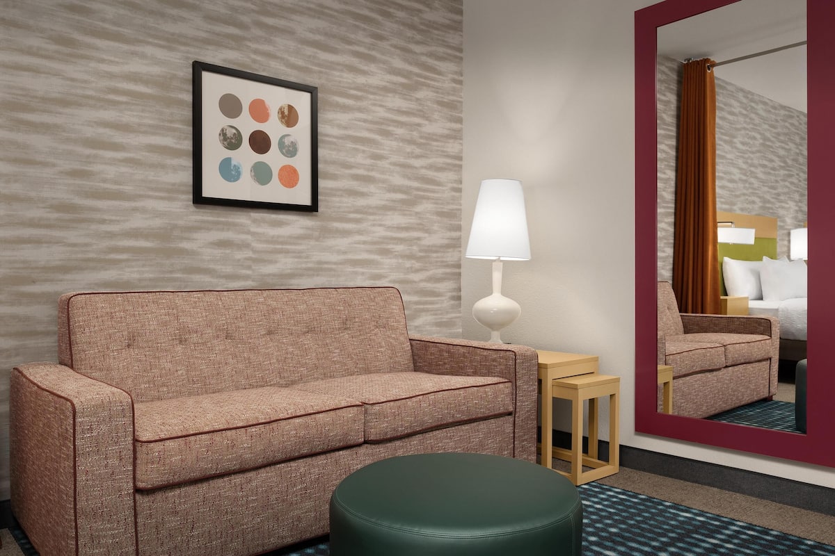 Une chambre d’hôtel avec un canapé, une petite table avec une lampe, un miroir et un tapis à motifs.