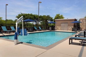 Ein Pool mit Liegestühlen und Sonnenschirmen, umgeben von einem Zaun und Bäumen.