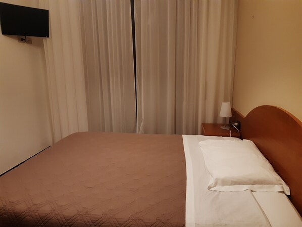 A hotel room with a bed, a nightstand, a lamp, and a flat-screen TV mounted on the wall. - Hotel Due Gemelli (Riomaggiore)