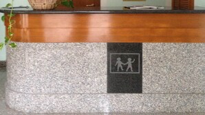 Un mostrador de recepción con una planta en maceta, una puerta de madera, un tablón de anuncios y un cartel con dos figuras.