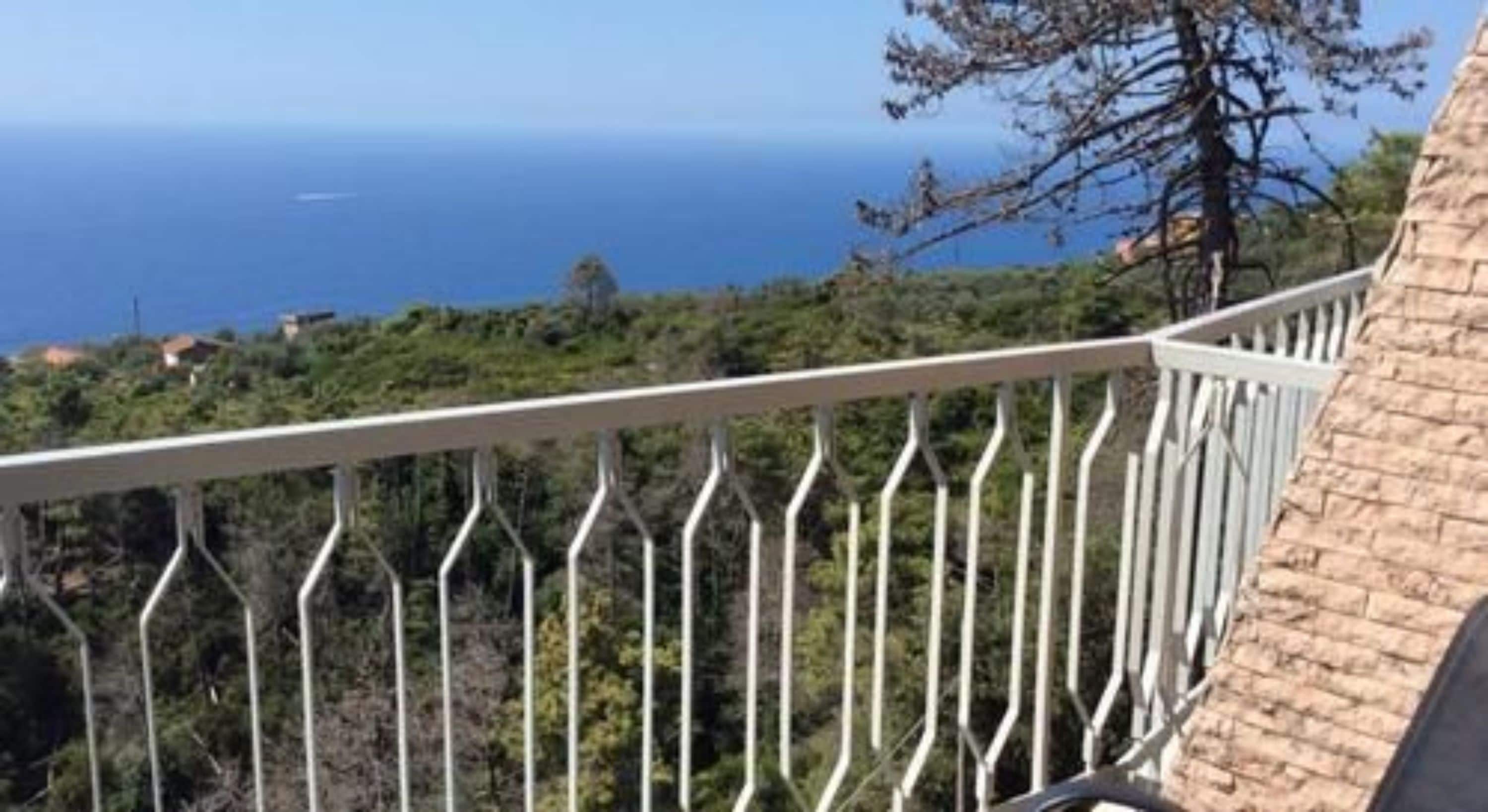 Un balcón con vista al mar y al verdor.