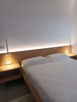 A modern bedroom with a wooden headboard, a bedside table with a lamp, and a bed with white bedding.