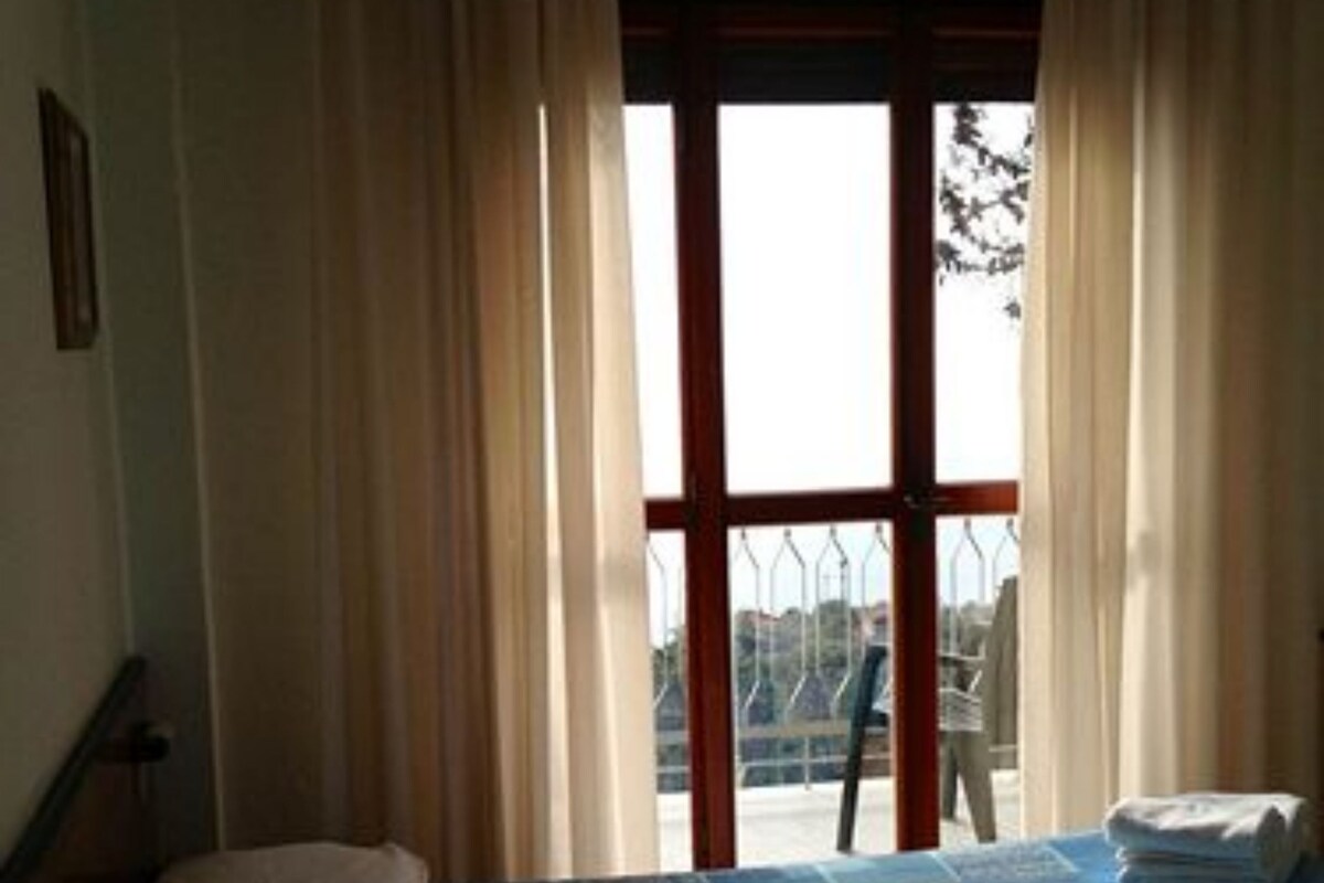 Una habitación con cama, ventana con cortinas y vista al exterior.