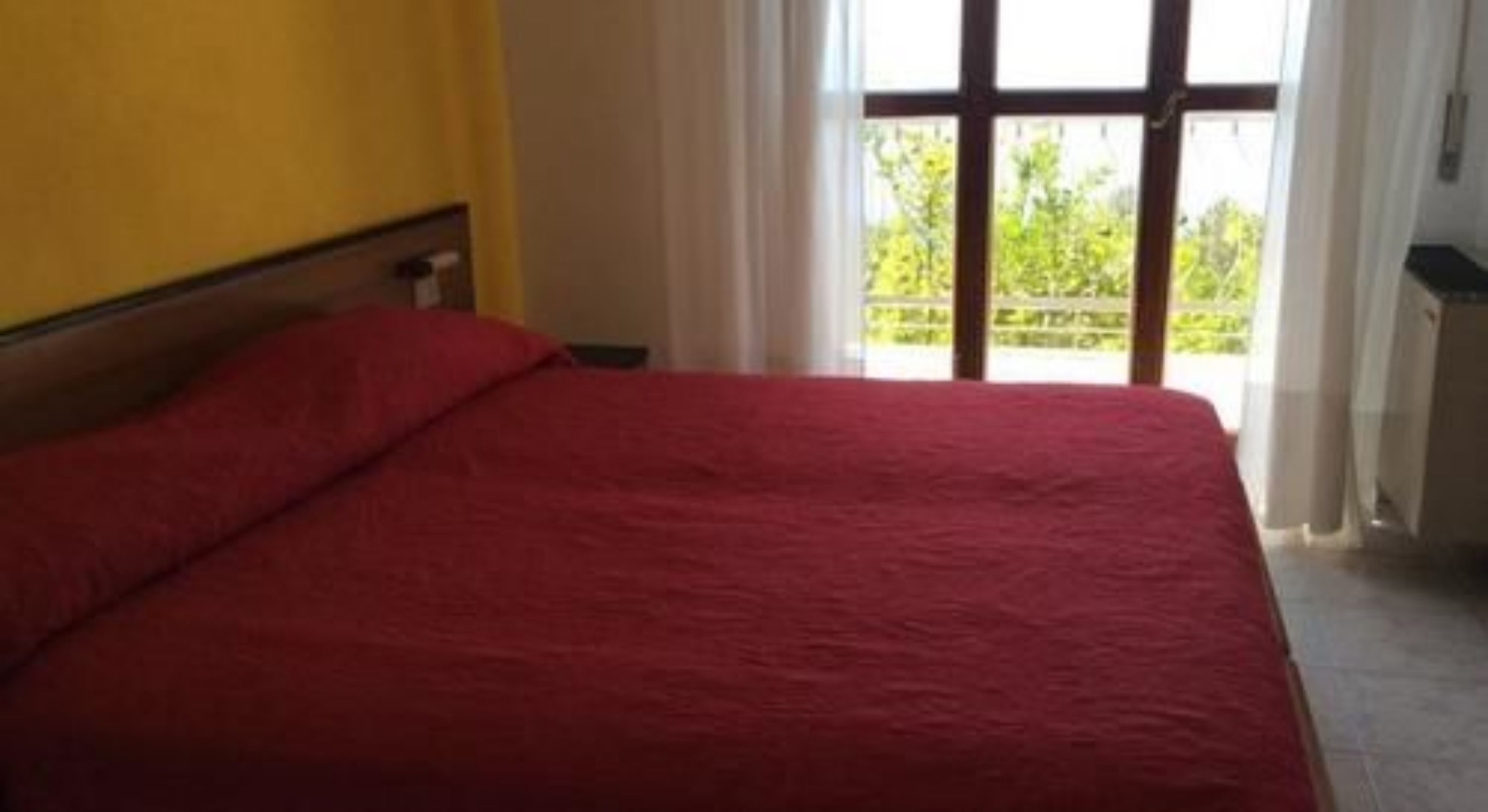Una cama con una colcha roja en una habitación con ventana.