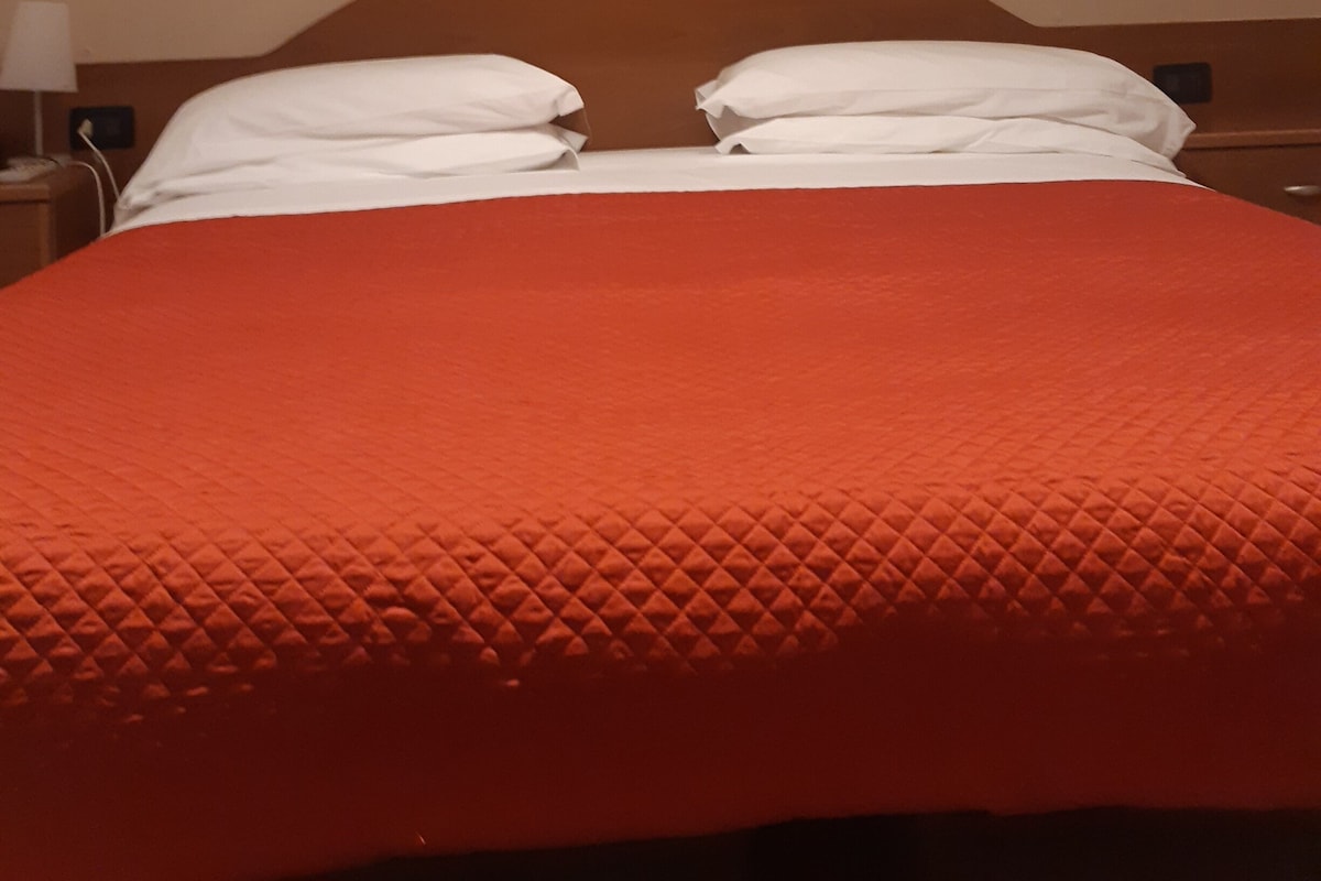 Una cama con colcha naranja, almohadas blancas y cabecera de madera.