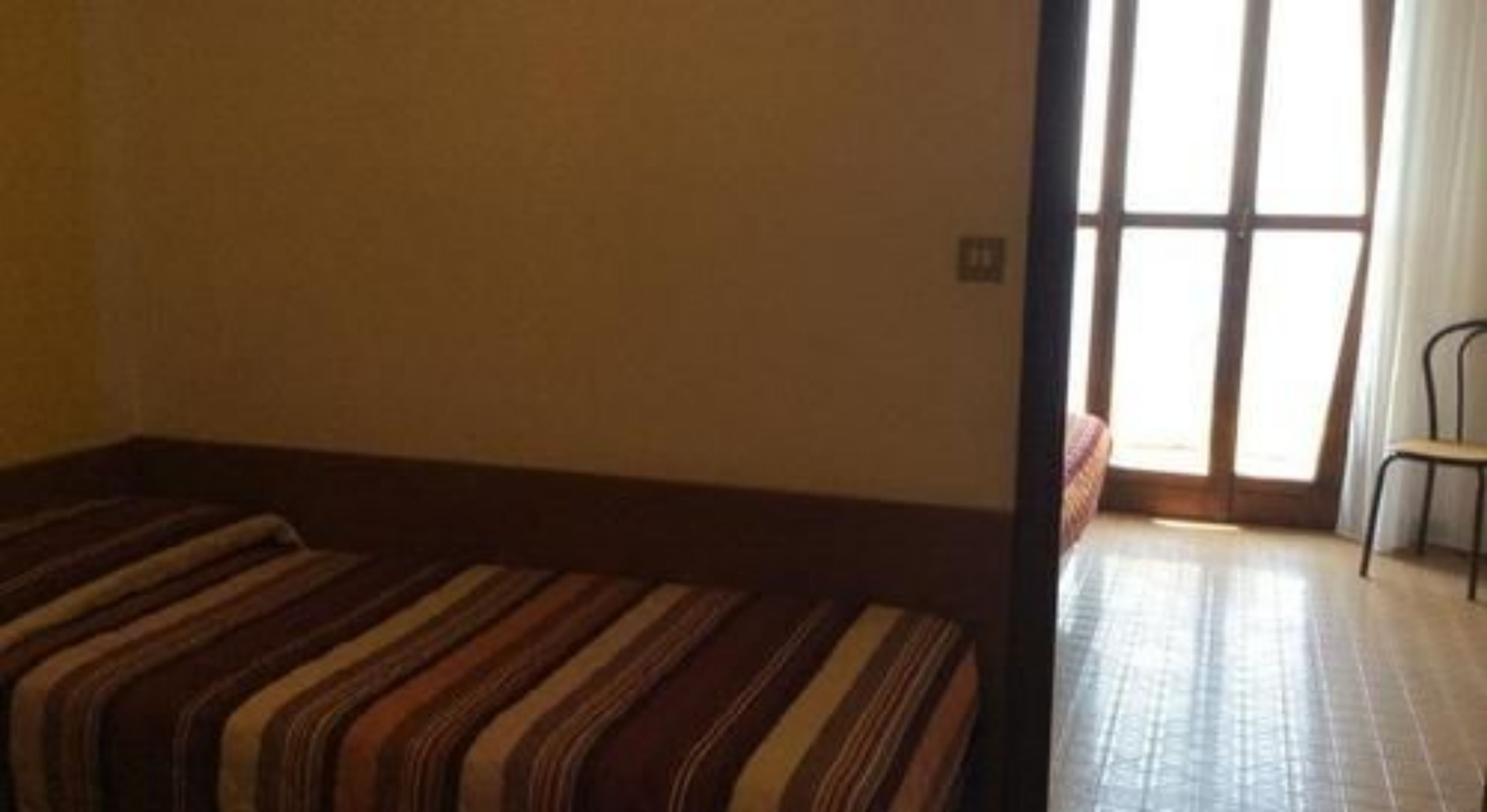 A room with a striped sofa, a chair, and a large window with curtains.
