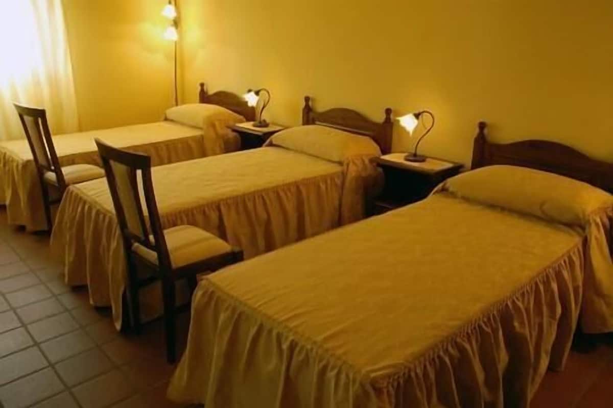 A hotel room with three single beds, each with a wooden headboard and a bedside lamp.