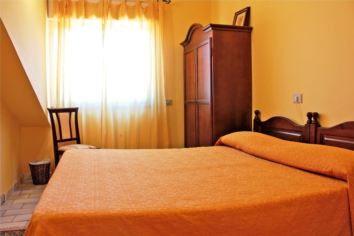 A bedroom with a bed, a wooden wardrobe, a chair, and a window with curtains.