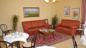 Ein Wohnzimmer mit zwei roten Sofas, einem Couchtisch, einem Esstisch mit Stühlen und einem gemusterten Teppich.