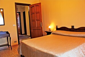A bedroom with a bed, a nightstand, a wooden door, and a desk.