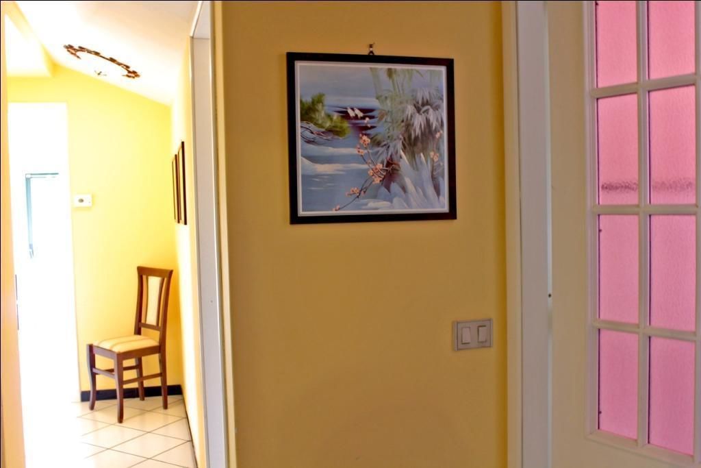 A hallway with a framed painting on the wall, a chair, and a door with pink-tinted windows.