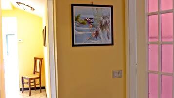 A hallway with a framed painting on the wall, a chair, and a door with pink-tinted windows.