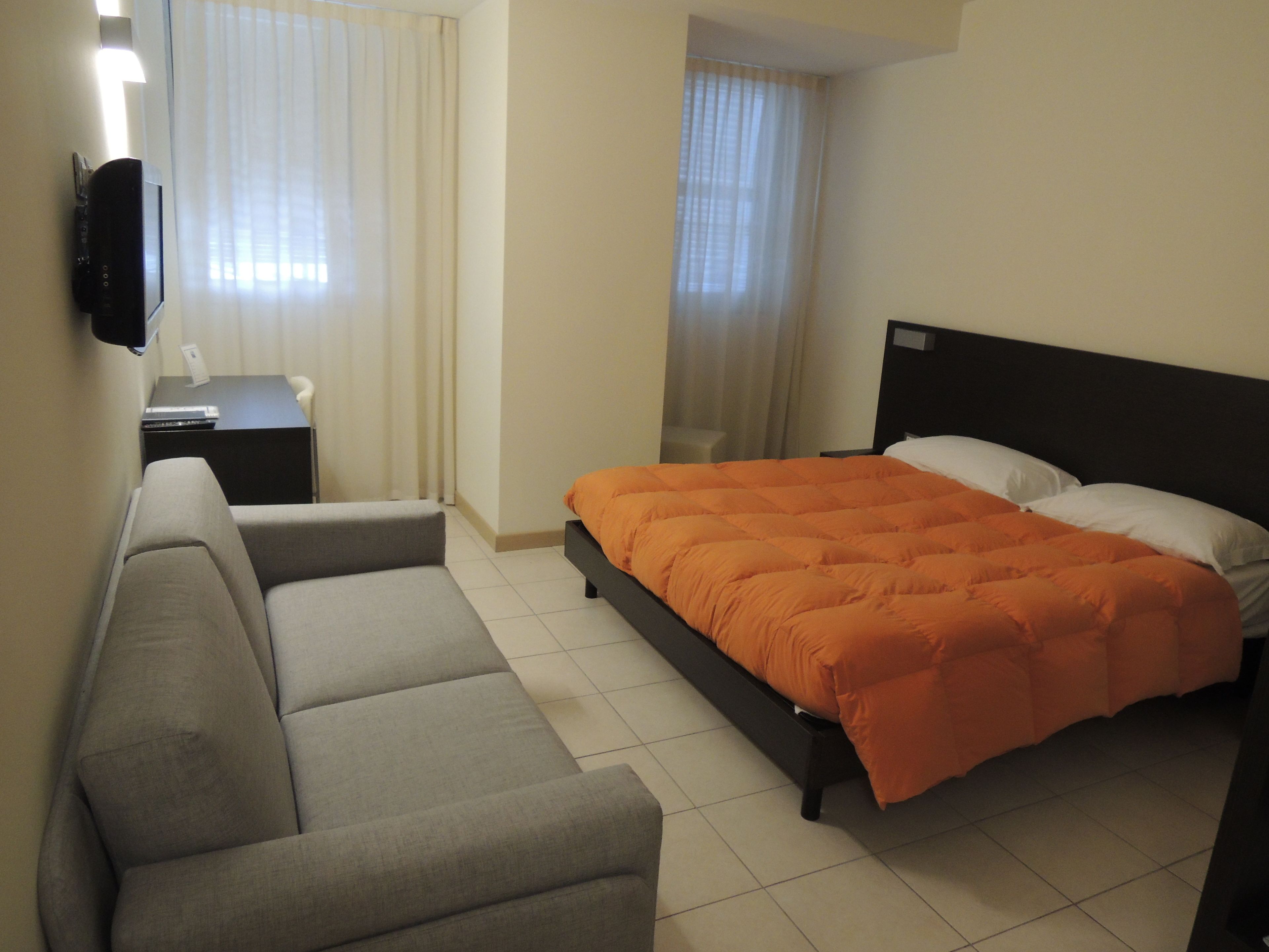 Ein Hotelzimmer mit Bett, Sofa, Schreibtisch und Fernseher.
