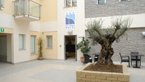 Hotellin sisäänkäynti, jossa on suuri istutusastia suurine puineen, ulkotila, jossa on istuimia, sekä kyltti, jossa lukee San Giorgio Hotel.