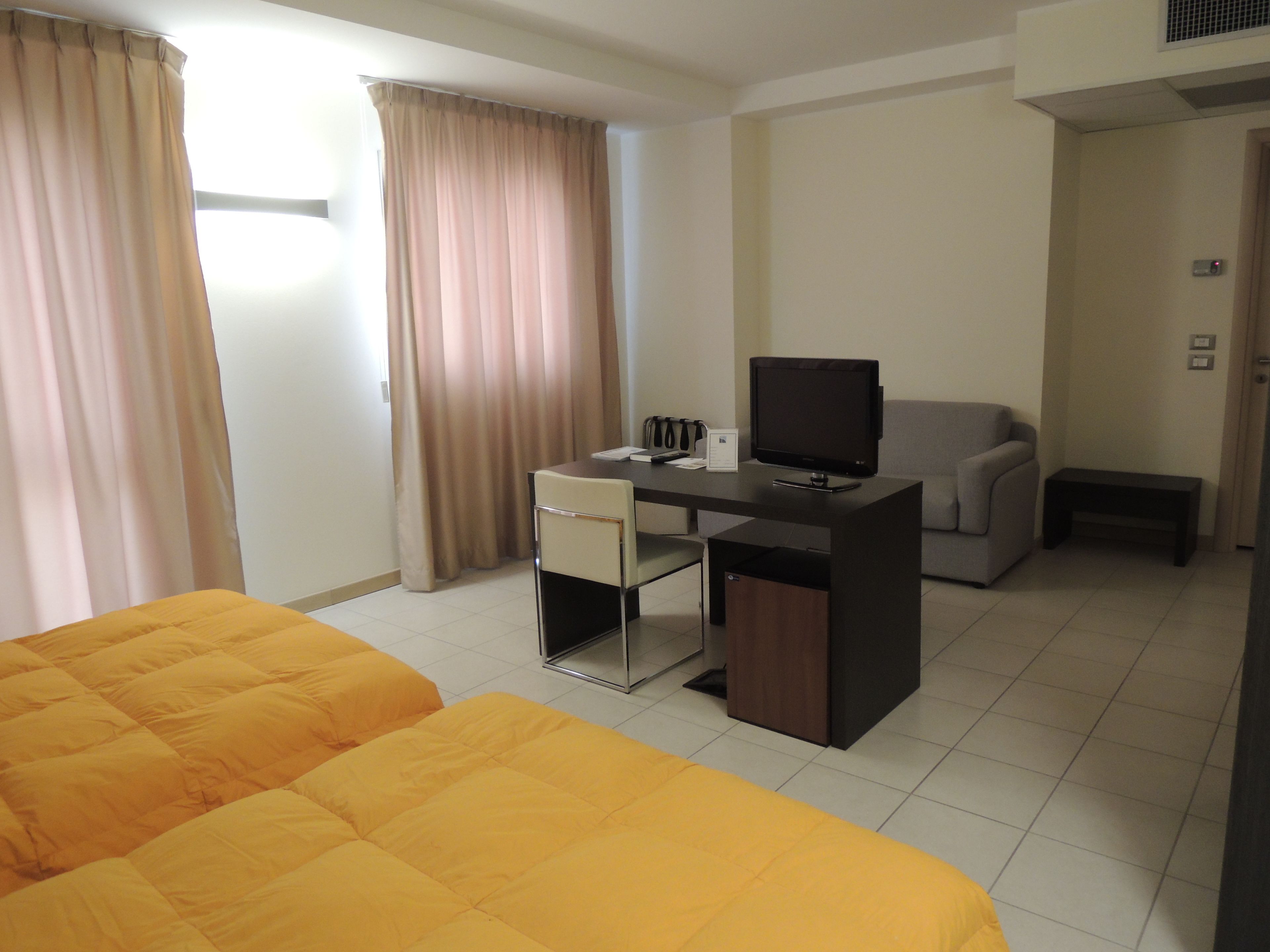 Ein Hotelzimmer mit zwei Betten, einem Schreibtisch mit Computer, einem Sessel, einer Couch und einem kleinen Tisch.