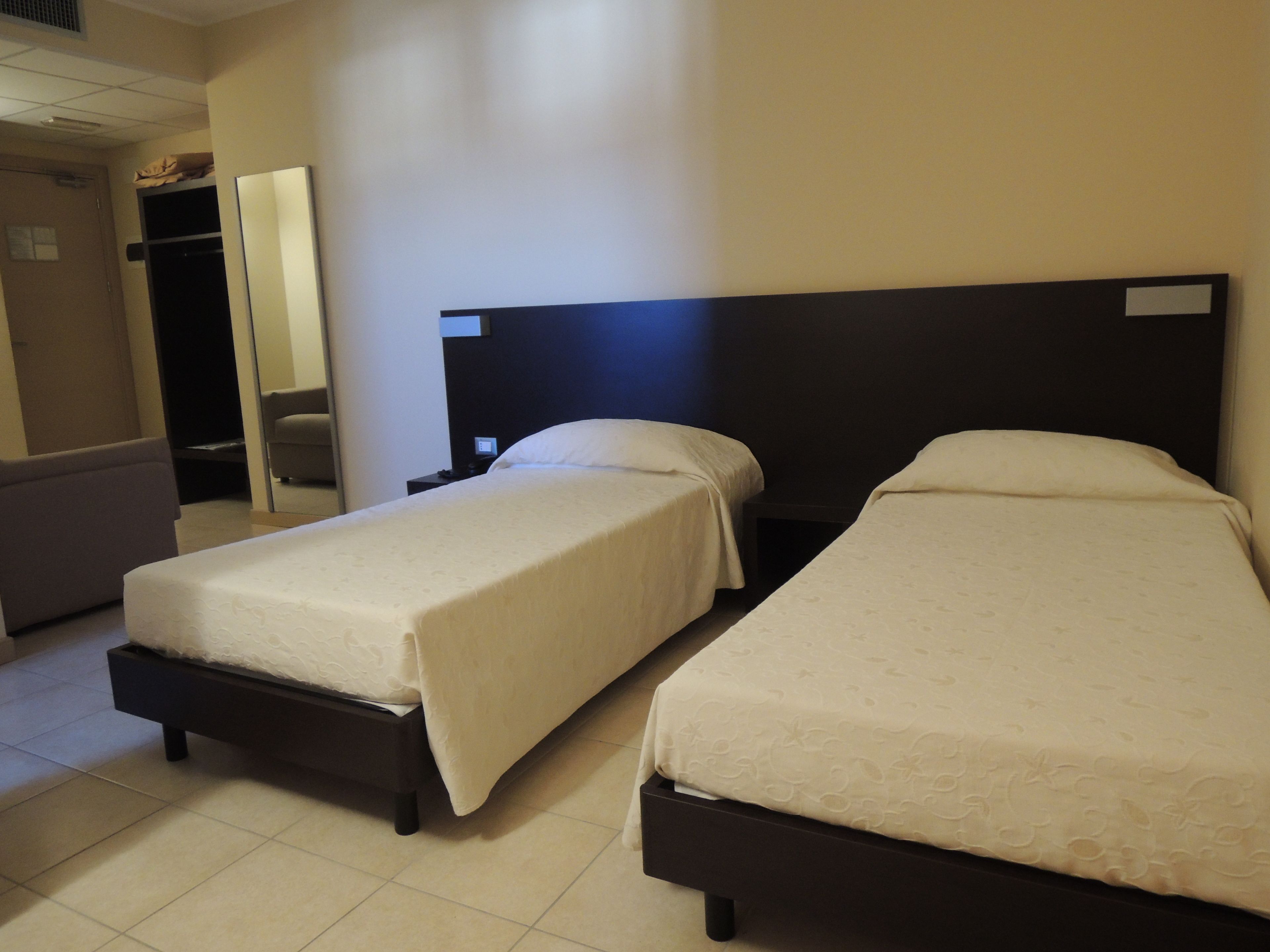 Une chambre d’hôtel avec deux lits simples, un petit canapé et un bureau avec une chaise.