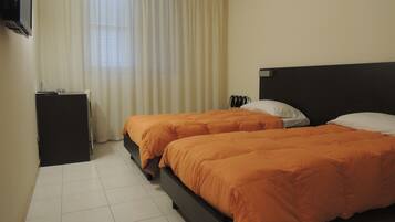 Habitación de hotel con dos camas, televisión, escritorio y ventana con cortinas.