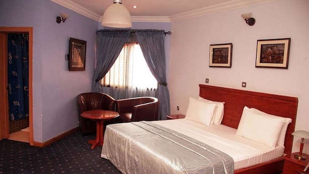 A hotel room with a bed, a desk, a chair, and a window with curtains. - Solitude Hotel Victoria Island (Lagos)