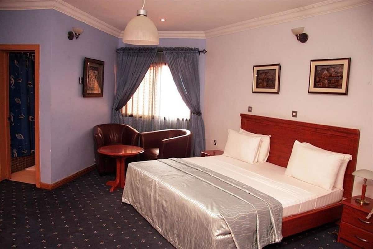 A hotel room with a bed, a desk, a chair, and a window with curtains.