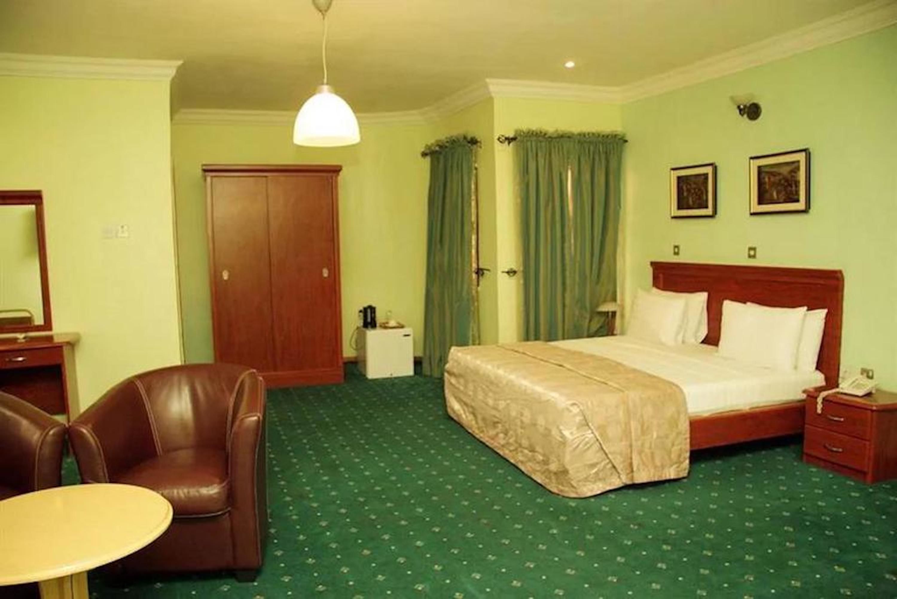 A hotel room with a bed, a chair, a desk, a wardrobe, and a small table.