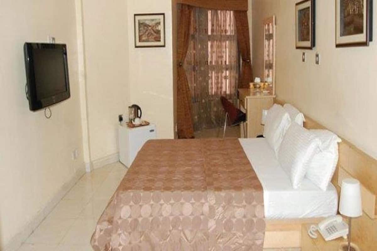 A hotel room with a bed, a TV mounted on the wall, a desk with a chair, and a window with curtains.