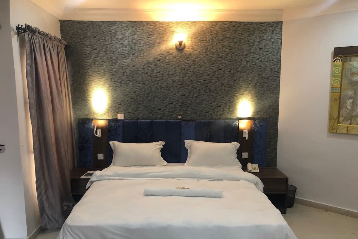 A hotel room with a bed, two bedside tables, a wall-mounted telephone, and a painting on the wall.