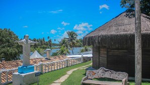 A statue, a bench, and a thatched-roof hut in a sunny outdoor setting. - Pousada Paradiso Tropical (Marechal Deodoro)