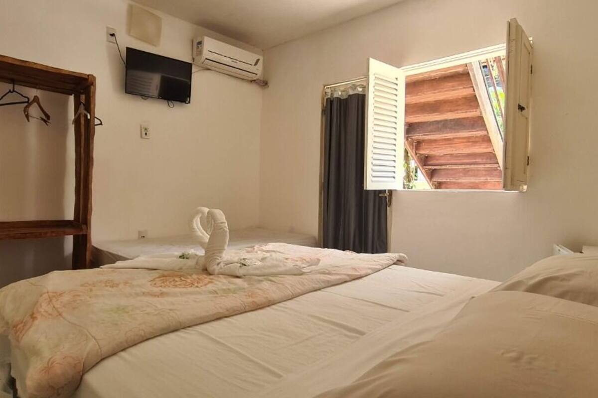 A bedroom with two beds, a wooden wardrobe, an air conditioning unit, and a window with curtains.