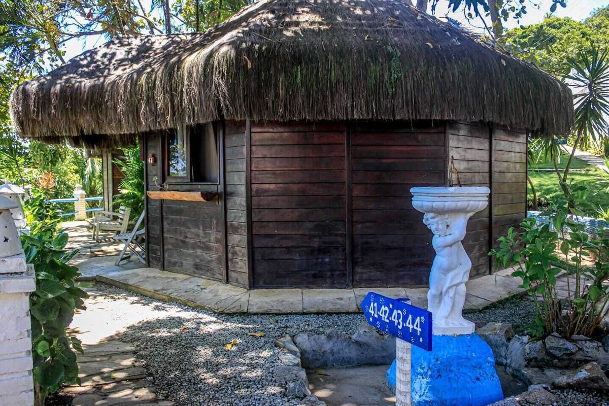 A small wooden hut with a thatched roof, a stone bench, and a decorative stone figure.