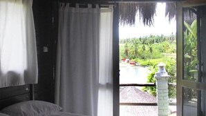 A room with a bed, white curtains, and a view of a lush landscape with a water body and greenery. - Pousada Paradiso Tropical (Marechal Deodoro)