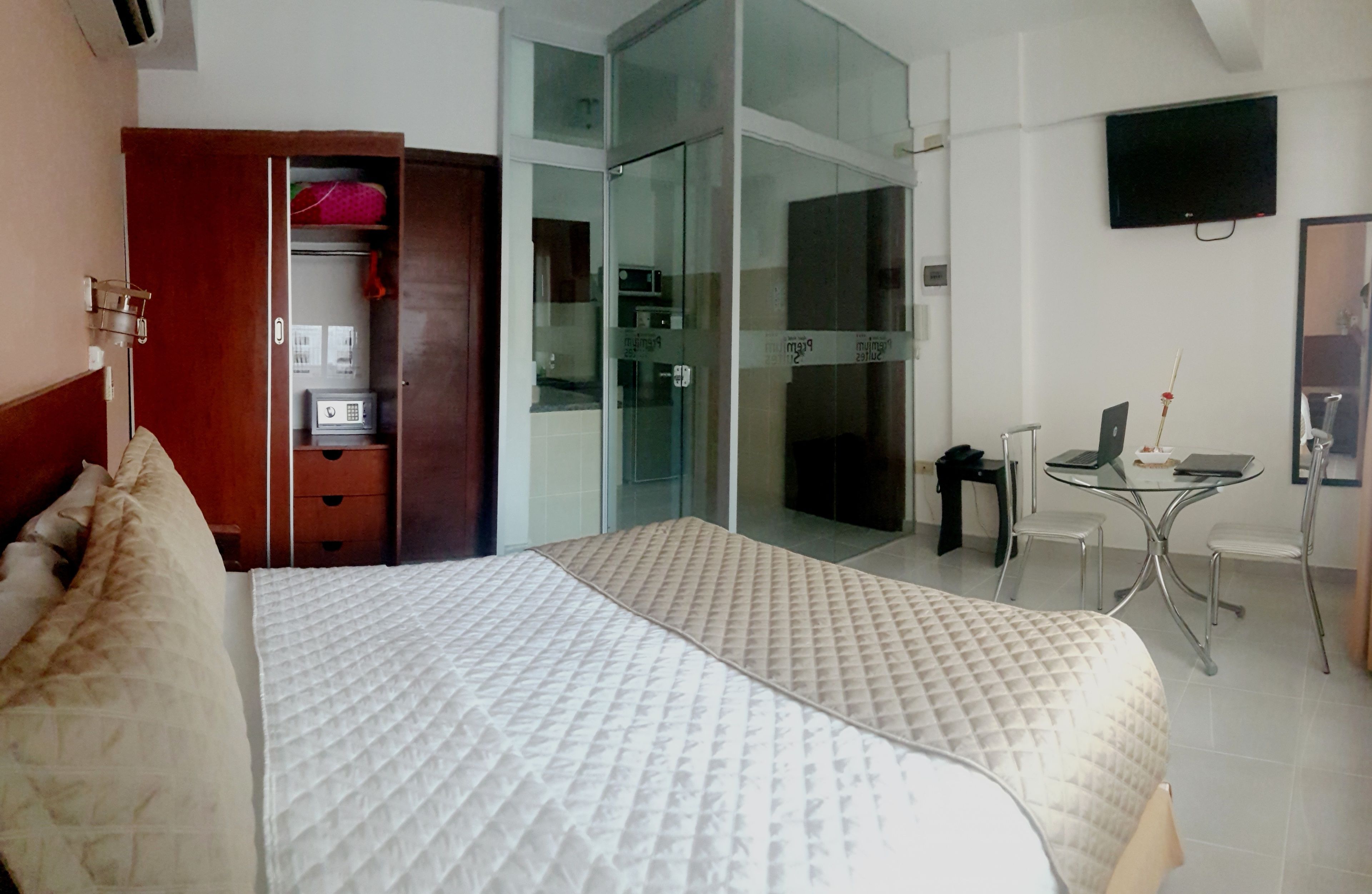 A hotel room with a large bed, a wardrobe, a desk, and a glass door leading to a bathroom.