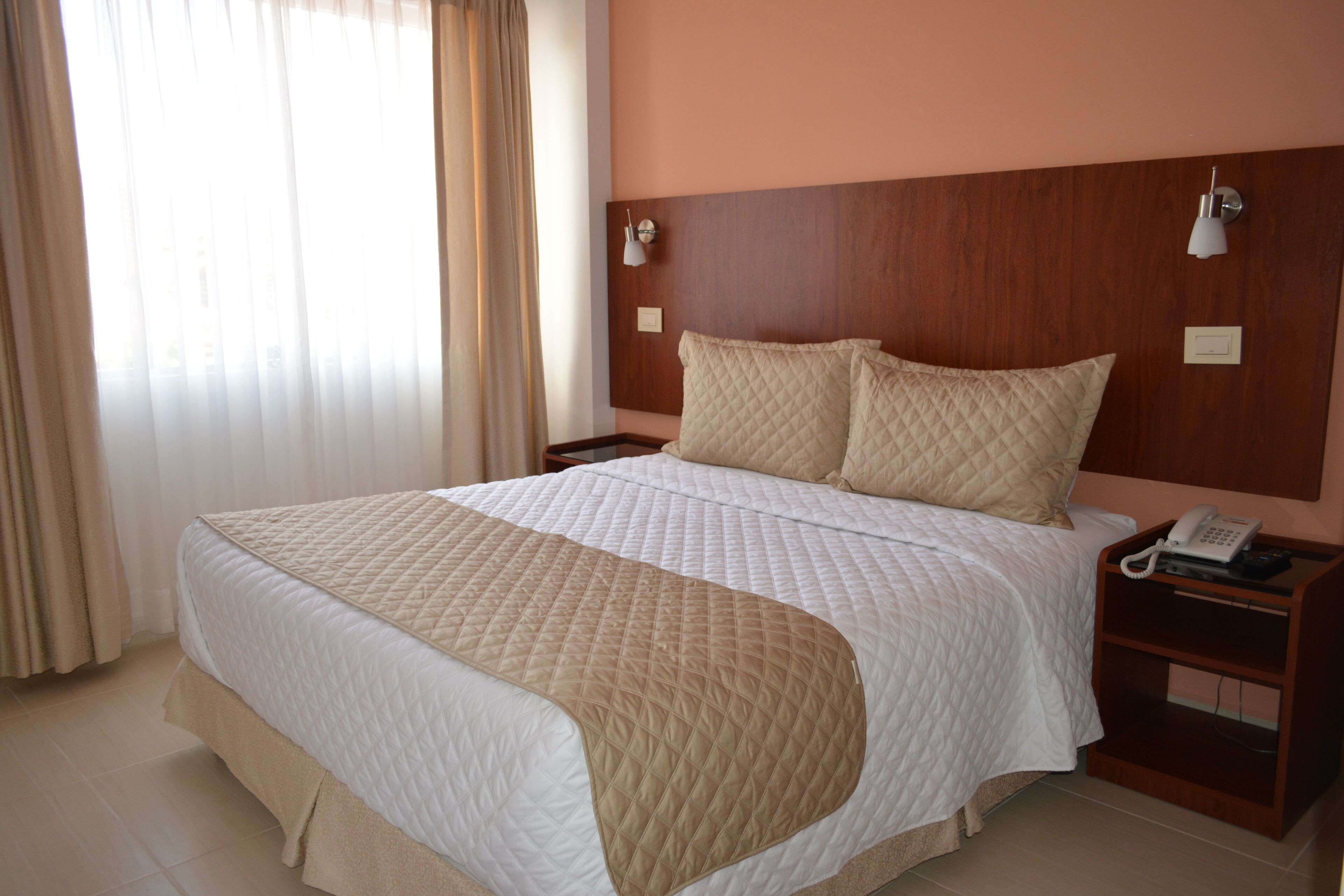 A hotel room with a large bed, wooden headboard, bedside lamps, and a bedside phone.