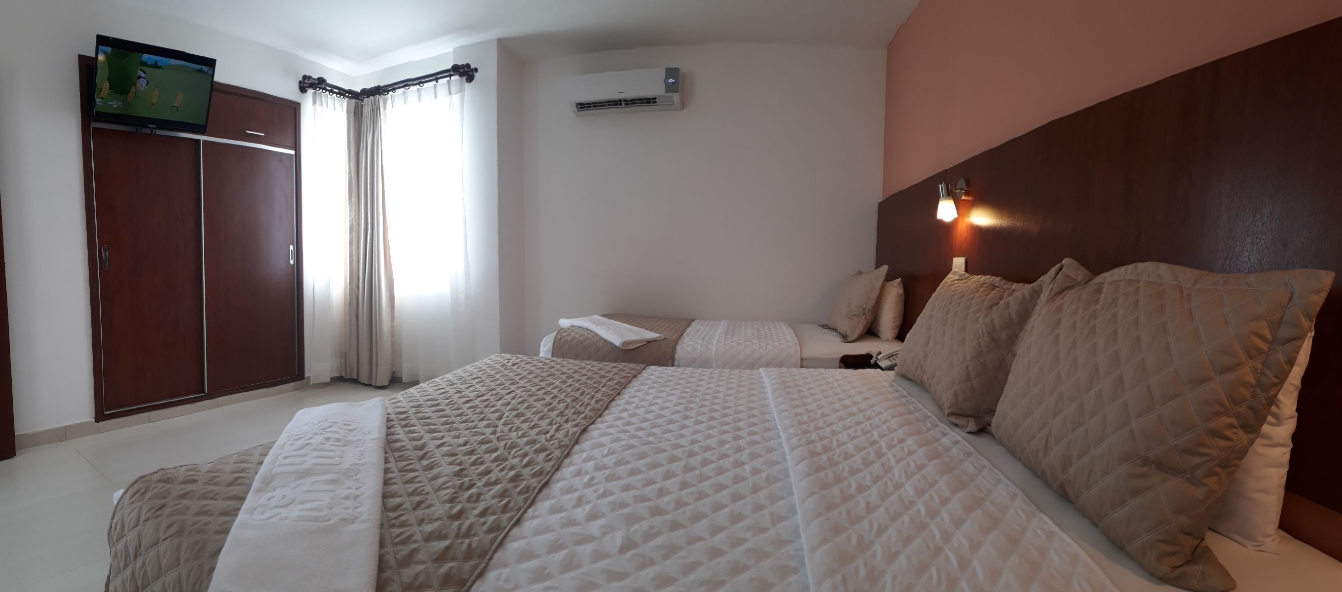 Quarto de hotel com uma cama grande, uma televisão na parede, guarda-roupa e unidade de ar condicionado.