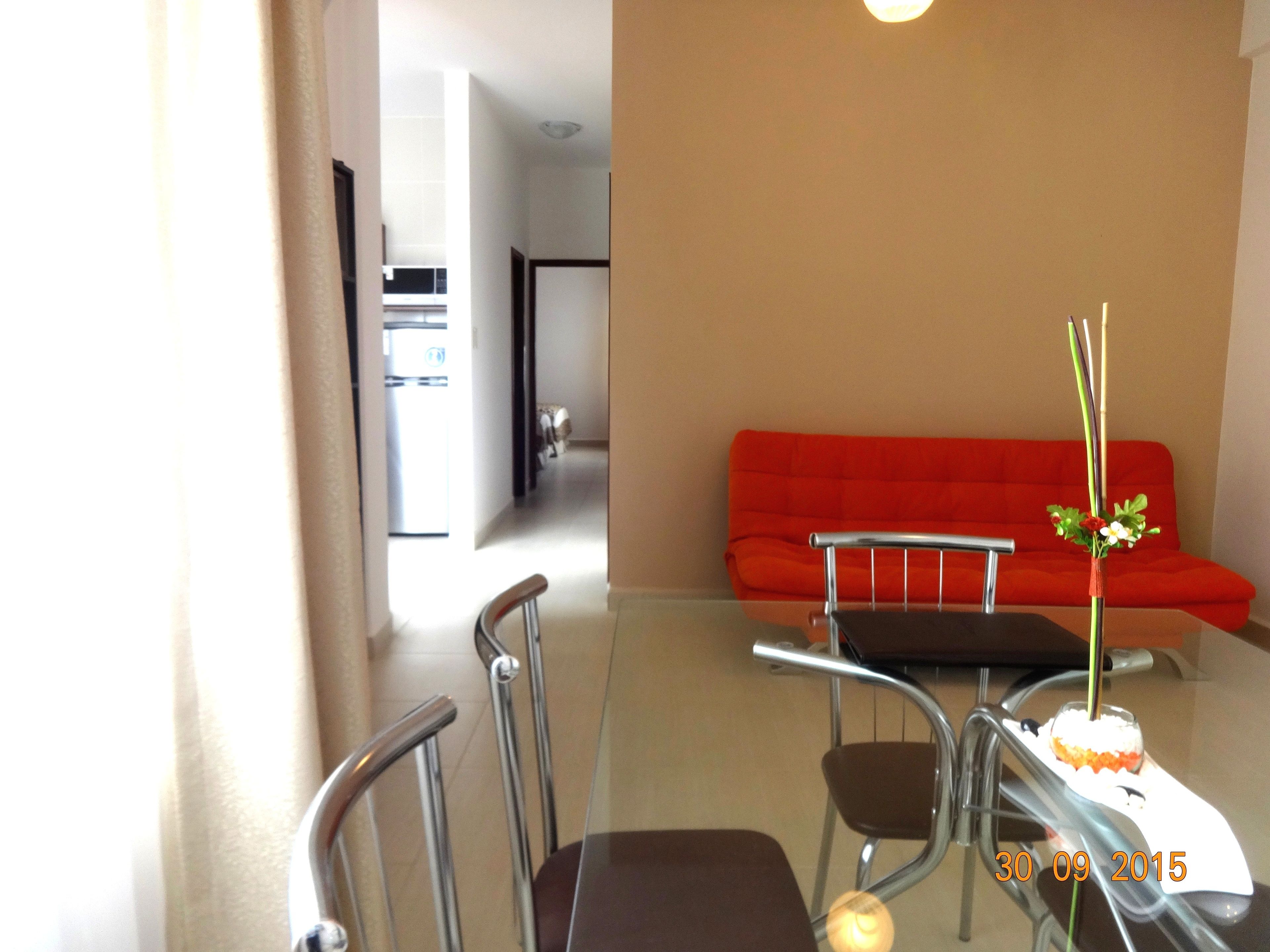 Un salon moderne avec une table à manger en verre, deux chaises, un canapé rouge et un vase rempli de fleurs.