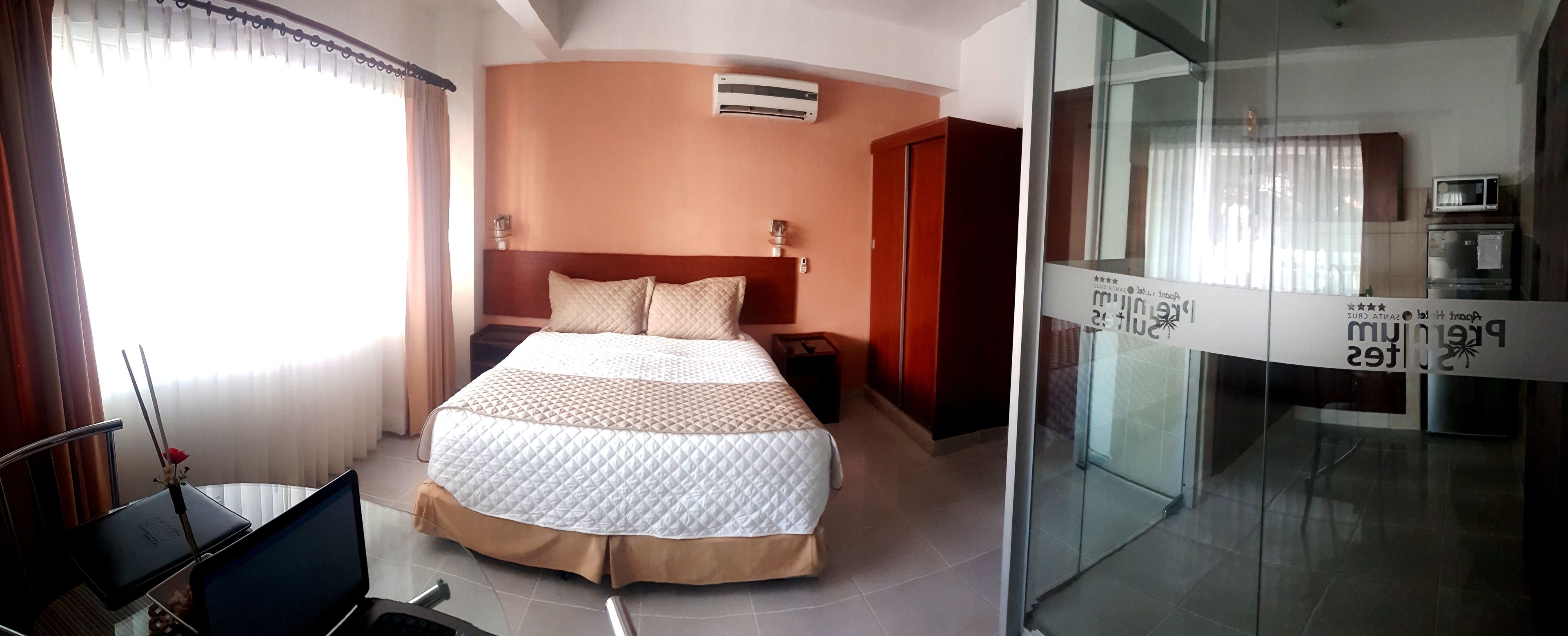 Ein Hotelzimmer mit Bett, Schreibtisch mit Laptop, Klimaanlage und Glastür zu einem Korridor.