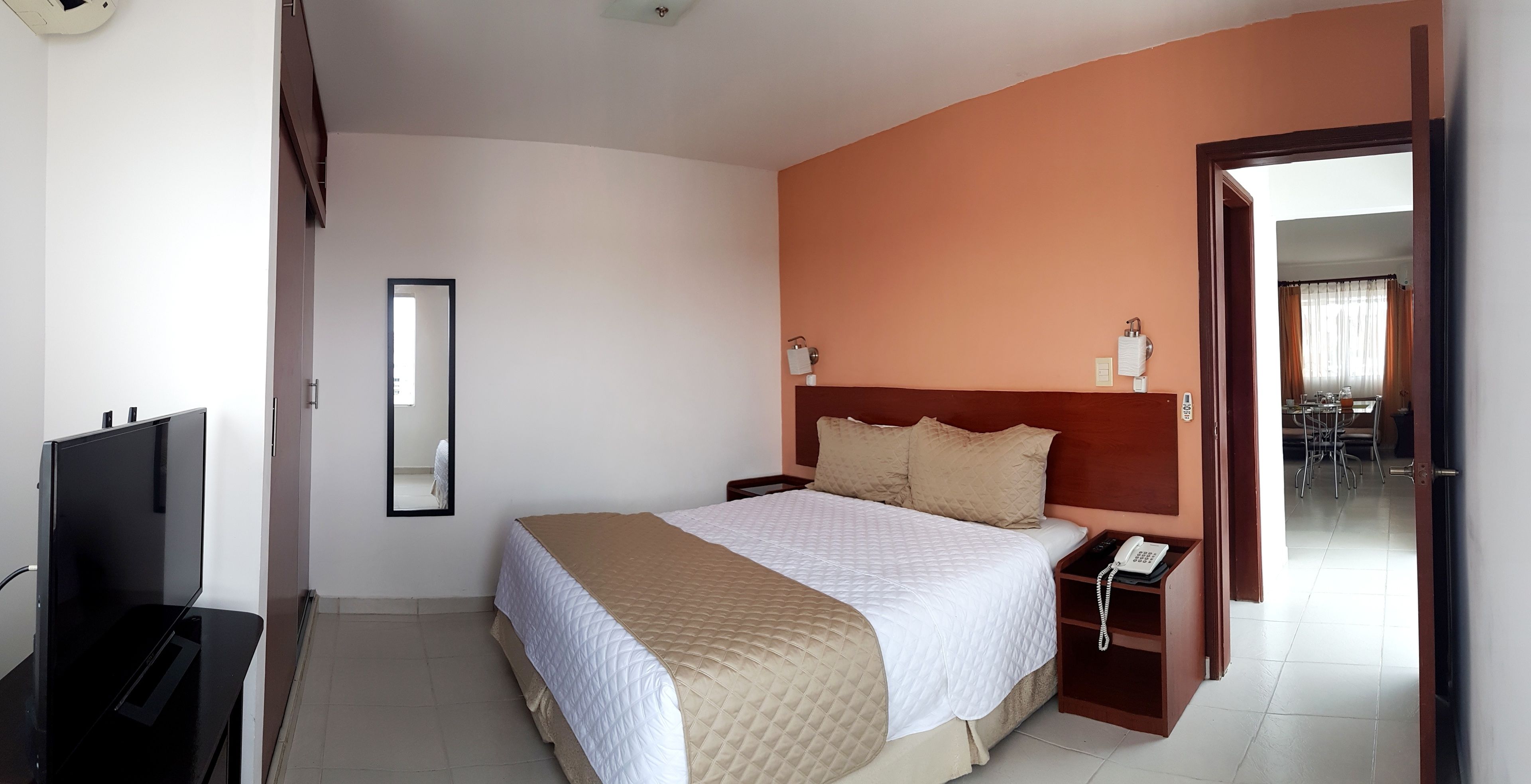 Una habitación de hotel con una cama, una mesita de noche con teléfono, un televisor y un espejo.