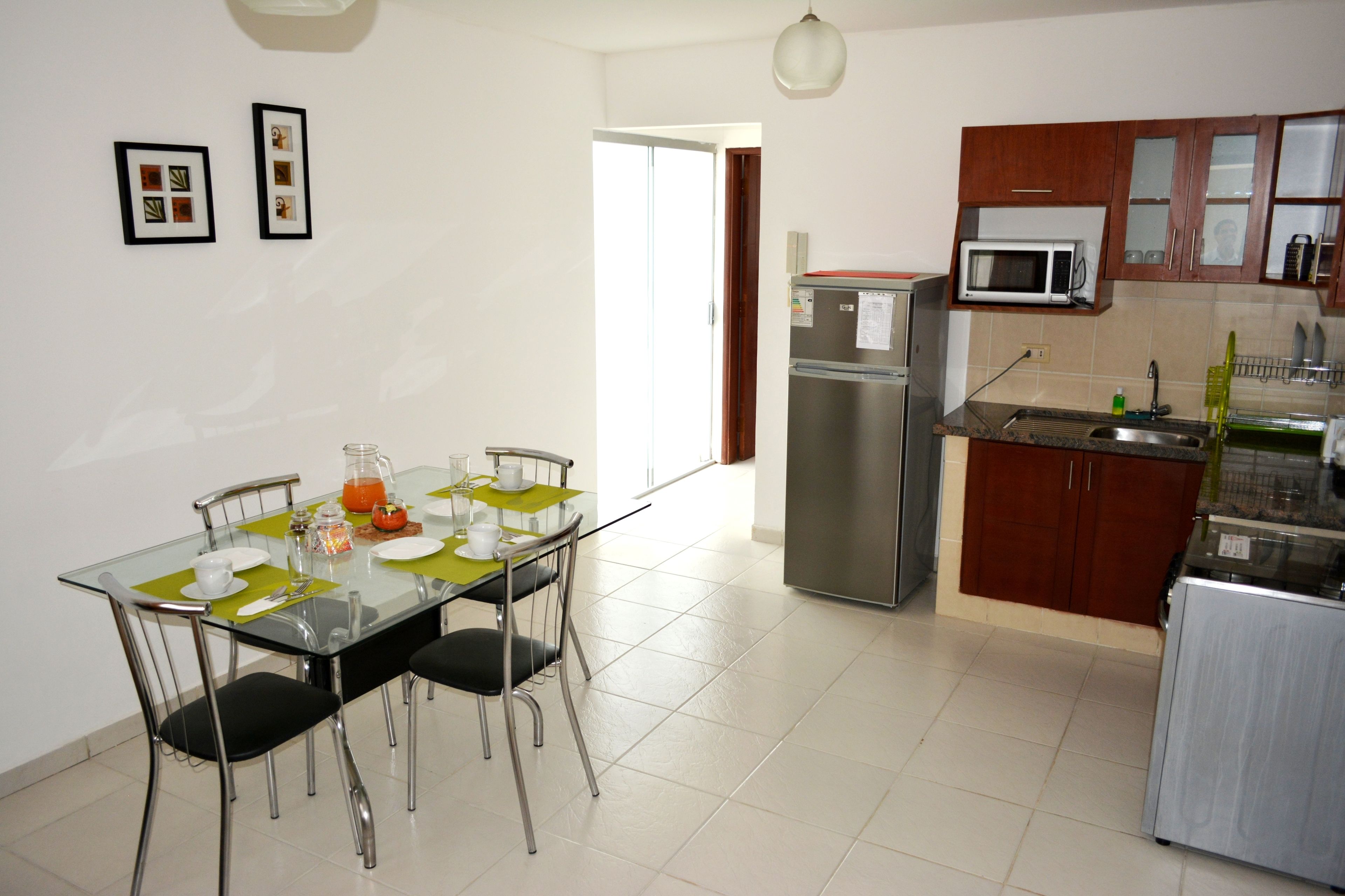 A modern kitchen with a refrigerator, microwave, and sink. There is a dining table with chairs and a glass top.