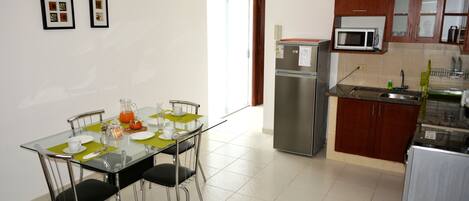 A modern kitchen with a refrigerator, microwave, and sink. There is a dining table with chairs and a glass top.