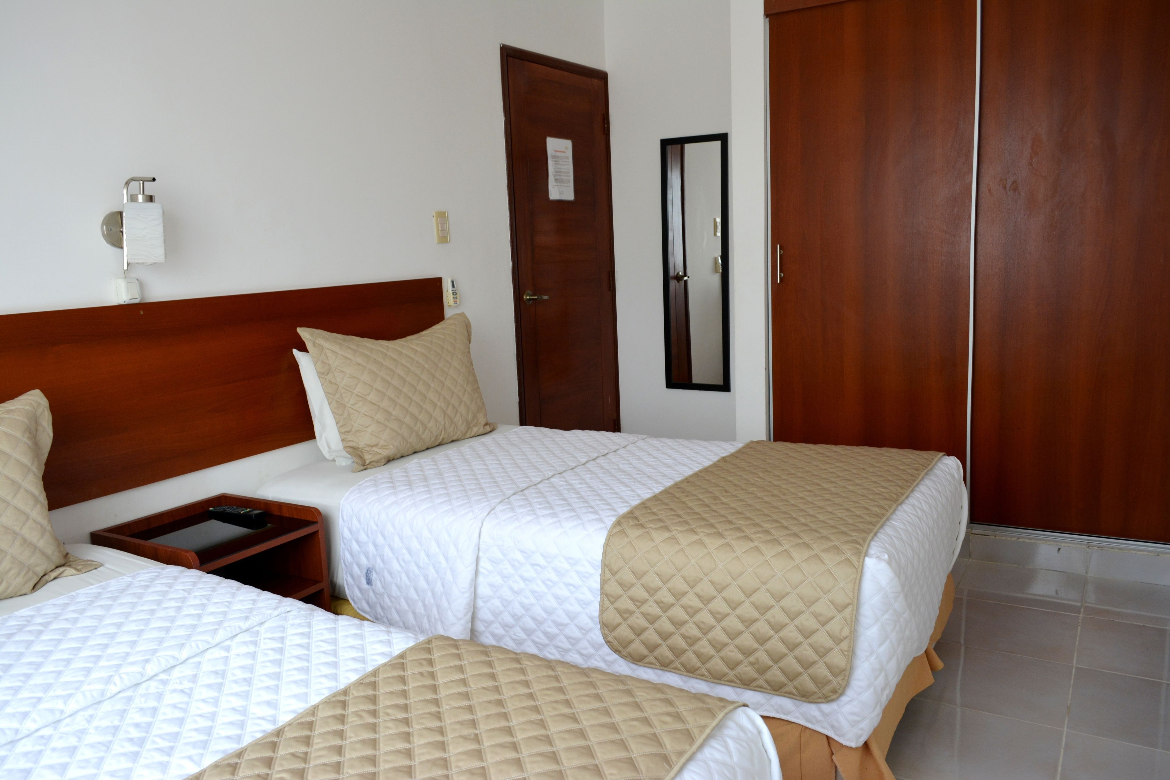 A hotel room with two beds, a wooden headboard, a nightstand, a mirror, and a wardrobe.
