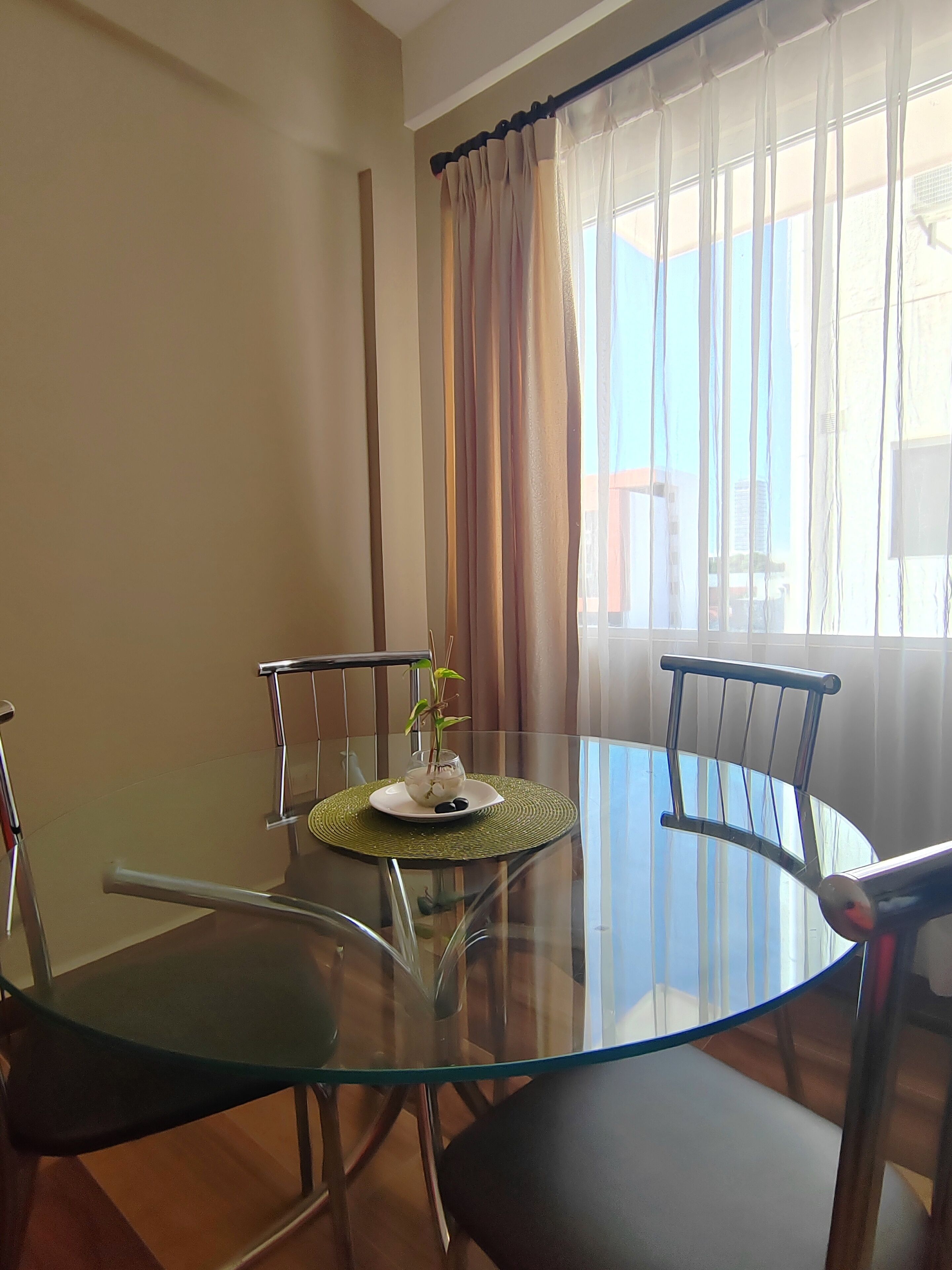 Un comedor con mesa de vidrio, sillas de metal y un florero con flores.