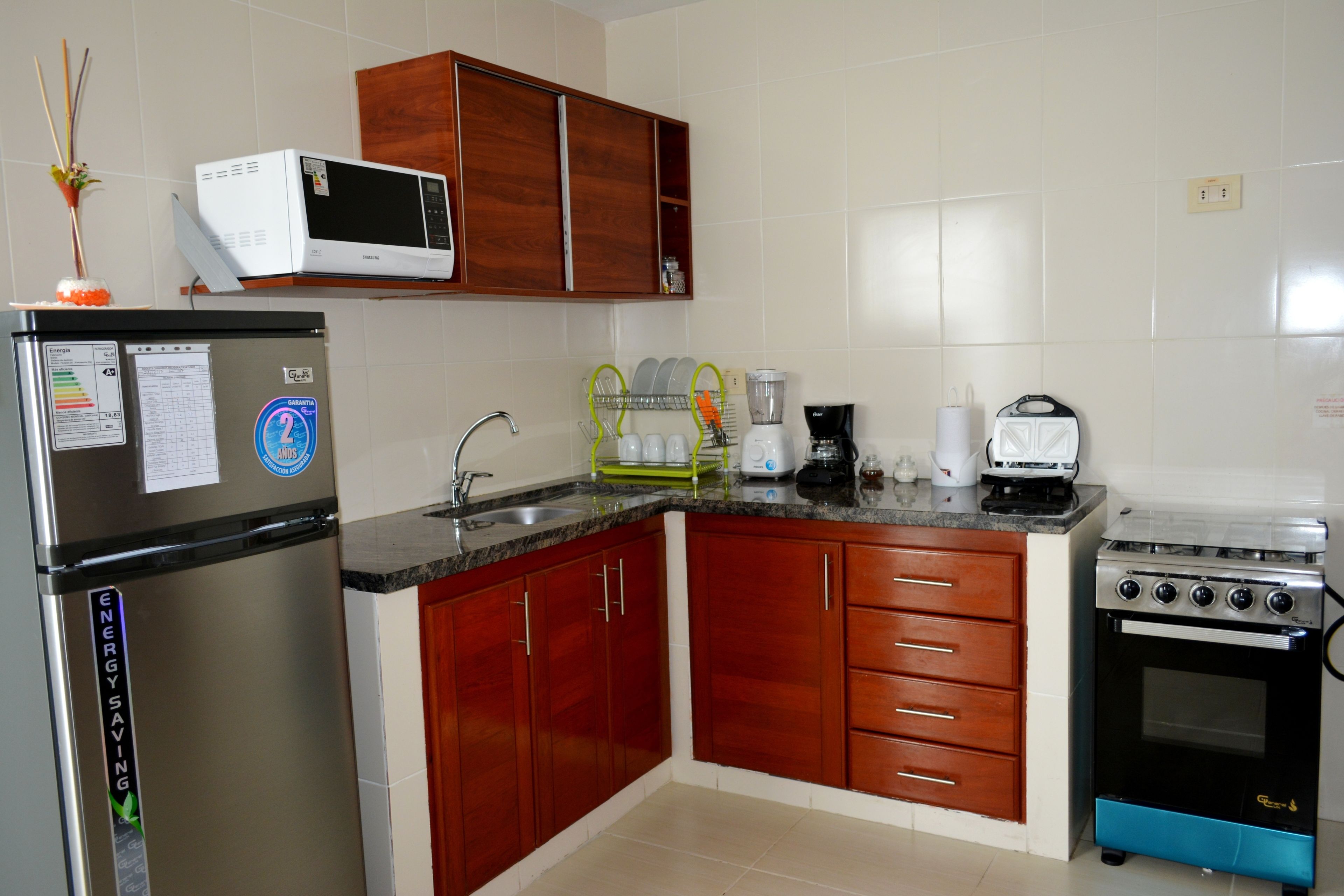 Een keuken met een koelkast, magnetron, kookplaat en diverse apparaten.