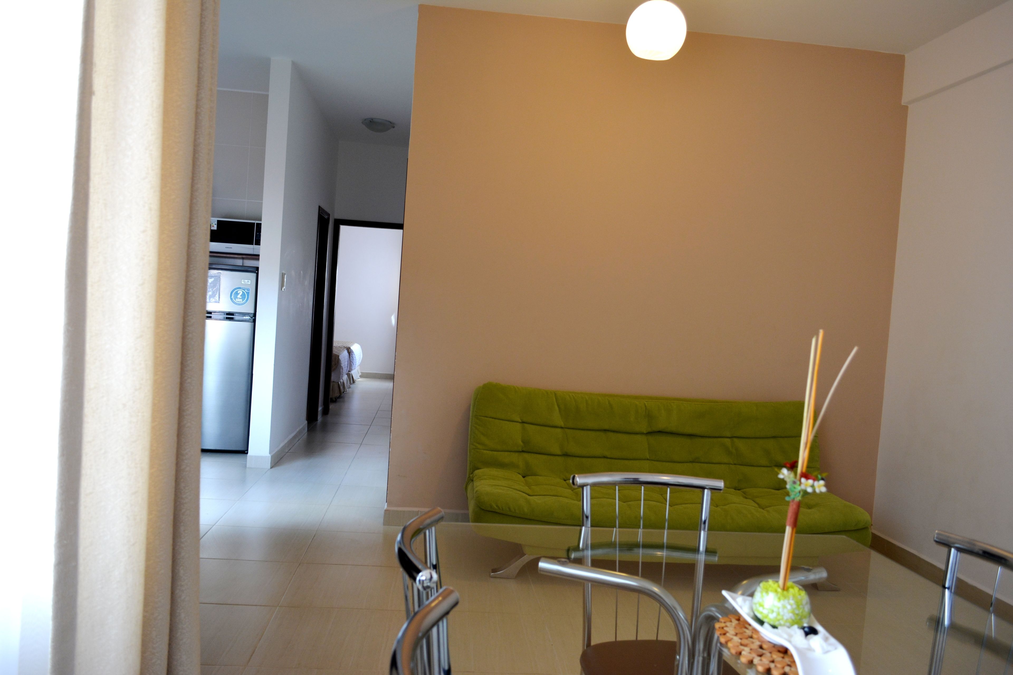 A modern living room with a green sofa, a glass-top coffee table, and a dining area with chairs.